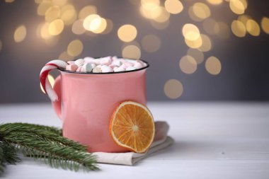 Lezzetli kakao, şekerleme kamışı, kurutulmuş portakal dilimi ve köknar dalı beyaz ahşap masa üzerinde bulanık Noel ışıklarına karşı, yakın çekim