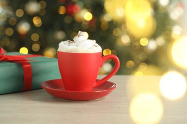 Krem şantili Aromatik kahve ve beyaz ahşap masada bulanık ışıklara karşı Noel hediyesi.