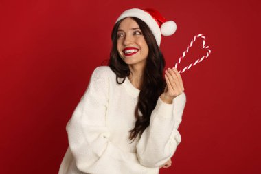 Kırmızı arka planda Noel Baba ve şeker kamışı olan güzel bir kadın. Noel sezonu