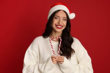 Kırmızı arka planda Noel Baba ve şeker kamışı olan güzel bir kadın. Noel sezonu