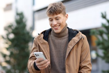 Şehirde akıllı telefonu olan ceketli, gülümseyen bir adam.