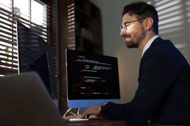 Ofiste çift monitörlü bilgisayar üzerinde çalışan gözlüklü programcı, düşük açılı görünüm