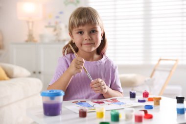 Beyaz masa içinde fırça çizen küçük kız.