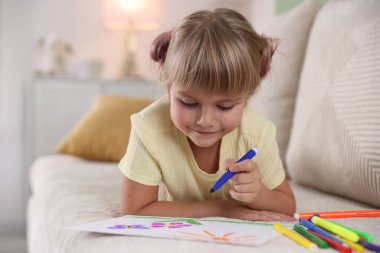 Evdeki kanepede keçeli kalemle çizen sevimli küçük kız.