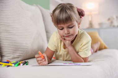 Evdeki kanepede keçeli kalemle çizen sevimli küçük kız.