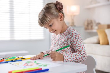 Beyaz masa içinde keçeli kalemle çizen sevimli küçük kız.