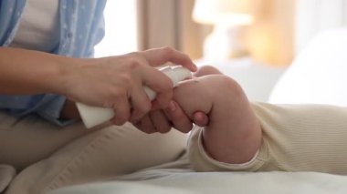 Anne evde bebeğinin bacağına krem sürüyor, yakın plan.