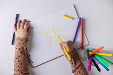 Beyaz masadaki keçeli kalemle çizen şirin küçük kız.