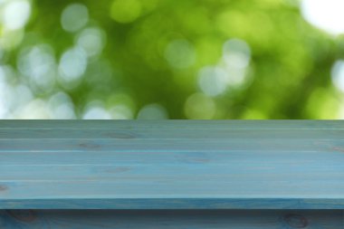 Dışarıdaki boş mavi ahşap masa. Arka planda bulanık yeşillik. Tasarım için boşluk