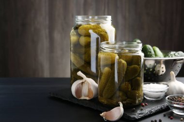 Kavanozdaki turşular, taze salatalıklar ve siyah tahta masadaki baharatlar, yakın plan. Metin için boşluk