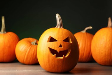 Cadılar Bayramı kutlaması. Koyu yeşil arka plana karşı ahşap masadaki farklı balkabakları