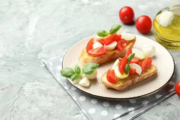 Mozzarella peynirli lezzetli bruschettalar, domates ve fesleğenli gri desenli masa, yakın plan. Metin için boşluk