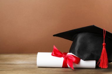 Mezuniyet şapkası ve diploması ahşap masada, kahverengi arka planda, yakın plan. Metin için boşluk