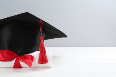 Mezuniyet şapkası ve diploması beyaz ahşap masada, arka planda ışığa karşı, yakın plan. Metin için boşluk