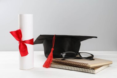 Mezuniyet şapkası, diploma, defterler ve gözlük beyaz ahşap masa ve arka planda. Metin için boşluk
