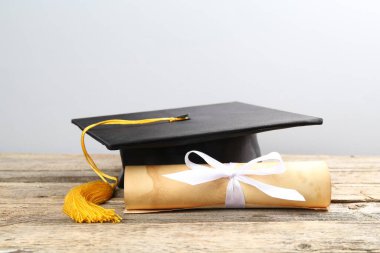 Mezuniyet şapkası ve diploması açık arkaplanda, ahşap masada.