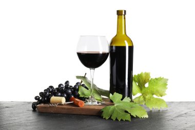 Bardakta kırmızı şarap, şişe, üzüm, tirbuşon ve yapraklar beyaz arka planda siyah masada.