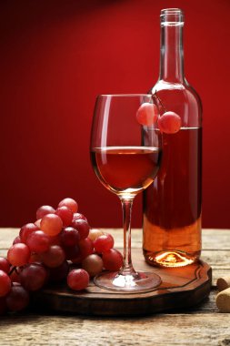 Cam, şişe ve üzümlü gül şarabı ahşap masada kırmızı arka planda, yakın planda.