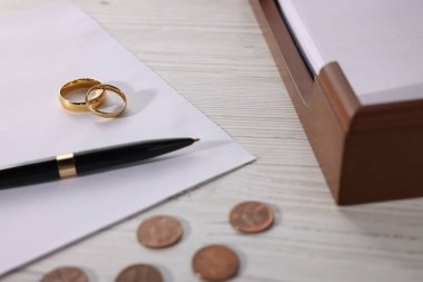 Nafaka. Bozuk paralar, kalemler, belgeler ve alyanslar ahşap masada, yakın plan.