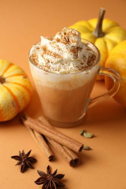 Krem şantili, baharatlı ve turuncu arka planda taze sebzeli balkabaklı latte. Yakın plan.