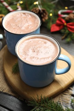 Bardaklarda lezzetli sıcak kakao ve karanlık ahşap masada Noel süsü, yakın plan.