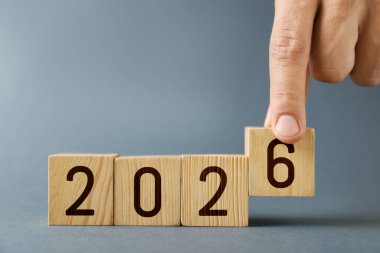 Yeni 2026 yılı. Adam gri arkaplana 6 numaralı küpü yerleştiriyor, yakın plan.