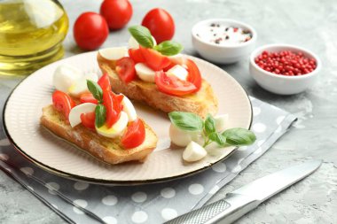 Mozarella peynirli, domatesli, fesleğenli ve baharatlı lezzetli bruschettalar. Gri desenli masa, yakın plan.