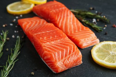 Somon filetosu, baharat ve limon parçaları siyah masada, yakın plan.