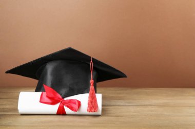 Mezuniyet şapkası ve diploması, kahverengi arka planla ahşap masada. Metin için boşluk