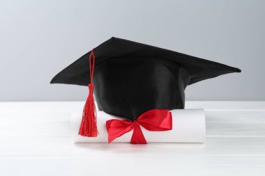 Mezuniyet şapkası ve diploması beyaz ahşap masada, arka planda ışığa karşı, yakın plan.