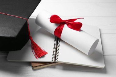 Mezuniyet şapkası, diploma ve defterler beyaz ahşap masa, yakın plan.