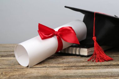 Mezuniyet şapkası, diploma ve defter ahşap masanın üzerinde, arka planda ışığa karşı, yakın plan.