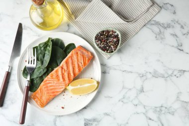 Lezzetli ızgara somon, limon dilimi ve beyaz mermer masada servis edilen ıspanak. Metin için boşluk
