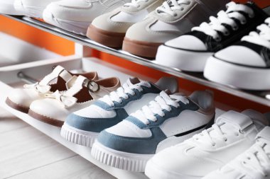 Turuncu duvarın yakınındaki raflarda farklı çocukların ayakkabıları var.