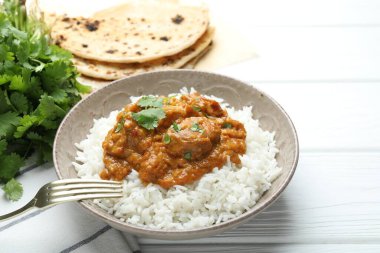Pirinçli lezzetli tavuk tikka masala, kişniş ve lavaş beyaz ahşap masada, yakın plan.