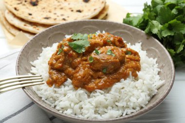 Pirinçli lezzetli tavuk tikka masala, kişniş ve lavaş beyaz ahşap masada, yakın plan.