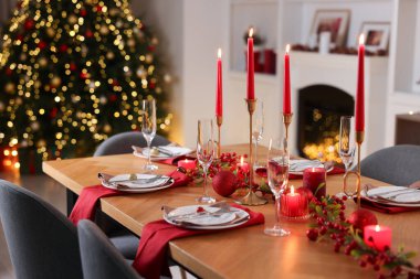 Şenlikli bir odada tabaklar, bardaklar ve yanan mumlarla şık bir Noel sofrası, yakın plan.