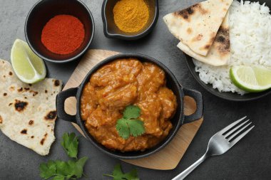 Lezzetli tavuk tikka masala, pilav, kişniş, kireç, lavaş ve baharatlar gri desenli masada, düz yerde.