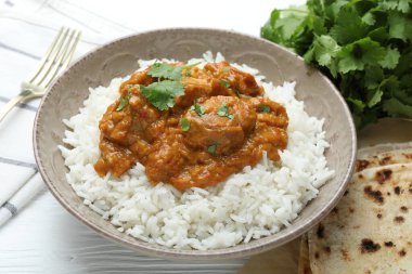 Pirinçli lezzetli tavuk tikka masala, kişniş ve lavaş beyaz ahşap masada, yakın plan.