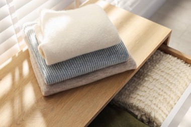 İçerideki pencerenin yanındaki dolapta temiz giysi yığını var.