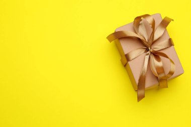 Sarı arka planda kurdeleli bir hediye kutusu, üst manzara. Metin için boşluk