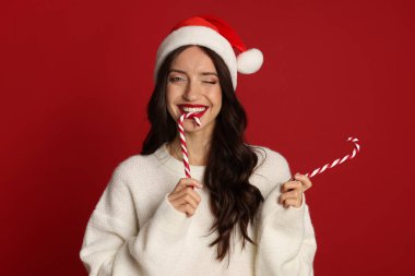 Kırmızı arka planda Noel Baba şapkası ve şeker kamışı olan güzel bir kadın. Noel sezonu