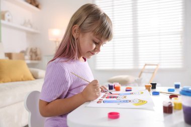 Beyaz masa içinde fırça çizen küçük kız.