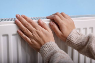 Kadın elini radyatörün yanında ısıtıyor, yakın plan.