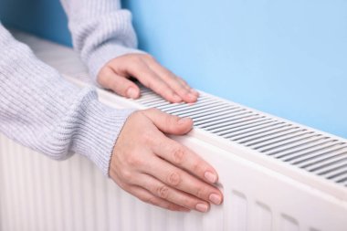 Kadın elini radyatörün yanında ısıtıyor, yakın plan.