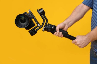 Sarı arkaplanda kameralı titreşim dengeleyici kullanan kameraman, yakın plan