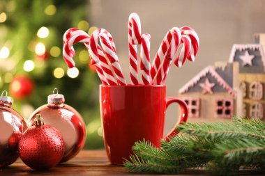 Kupada baston şekerler ve ahşap masada bulanık ışıklara karşı Noel süsü.