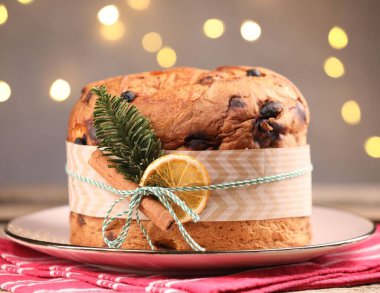 Baharatlı ve köknar dallı lezzetli bir Noel panettone pastası. Ahşap masa üzerinde, arka planda bulanık ışıklar ve yakın plan. Bokeh etkisi