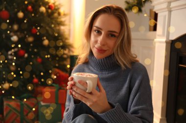 Odada Noel ağacının yanında bir fincan kakaolu güzel bir kadın var.