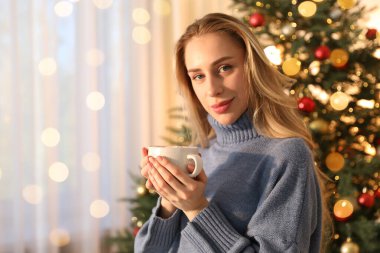 Odada Noel ağacının yanında bir fincan kakaolu güzel bir kadın var.